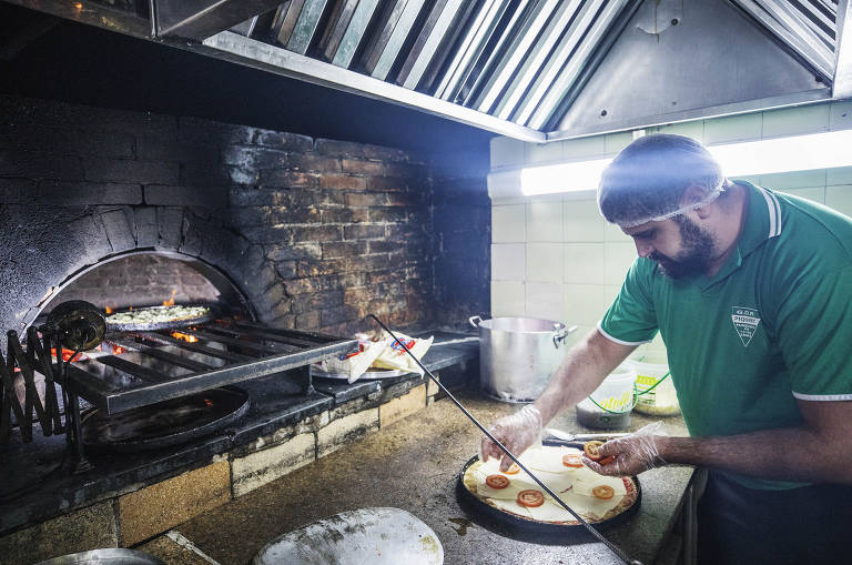 O pizzaiolo Leandro Ramon,32, monta pizza para assar e fritar na cozinha do clube