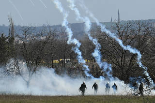 Greek riot police officers stand guard as tear gas is being fired near Turkey's Pazarkule border crossing, in Kastanies