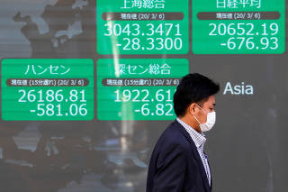 A passerby wearing a protective face mask, following an outbreak of the coronavirus, walks past an electronic display showing Asian markets indices outside a brokerage in Tokyo