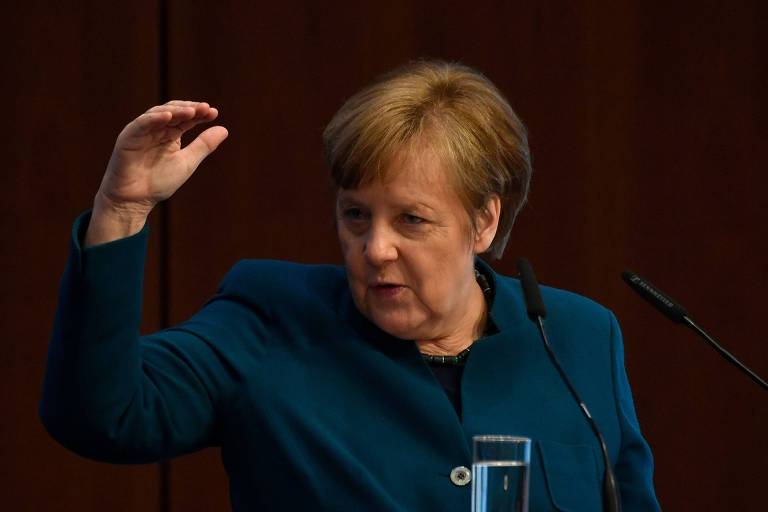 De roupa verde escuro, Merkel gesticula com a mão direita