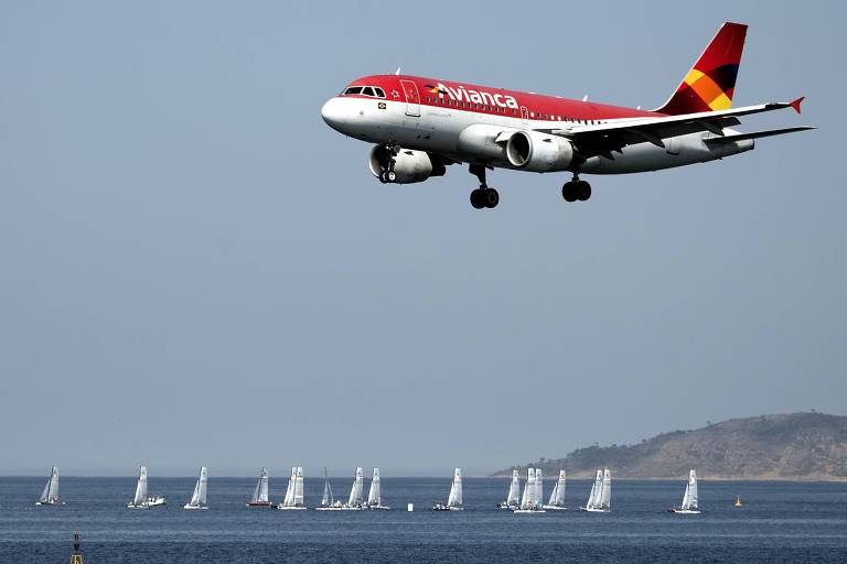 Imagem mostra avião vermelho da Avianca bem próximo à pista. No fundo há velas no mar e um morro.