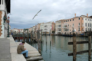 A man sits at a virtually deserted Grand Canal in Venice as the Italian government continues restrictive movement measures to combat the coronavirus outbreak, in Venice