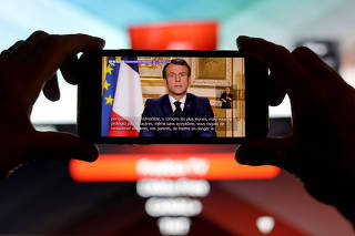 French President Emmanuel Macron is seen addresses the nation about the coronavirus disease (COVID-19) outbreak, on a mobile screen in this illustration picture