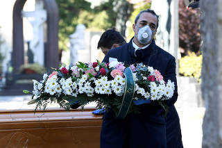 FILE PHOTO: Cemetery workers and funeral agency workers in protective masks transport a coffin of a person who died from coronavirus disease (COVID-19), into a cemetery in Bergamo