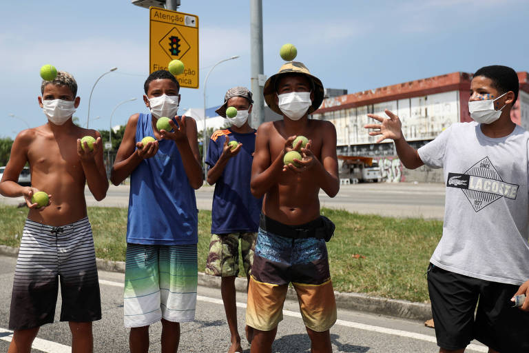 Grupo de quarto rapazes faz malabarismos com bolas de tênis; um quinto jovem os observa. Todos eles usam máscaras cirúrgicas para proteger o rosto.