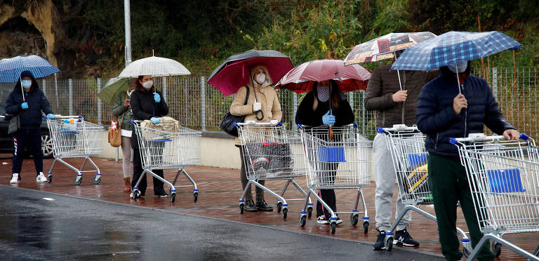 Sob chuva, pessoas fazem fila do lado de fora de um supermercado em Catânia, na região da Sicília

