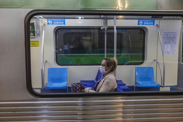 Imagem de uma mulher usando máscara dentro de um vagão de metrô. Ela está sozinha no vagão, sentada perto da janela. O rosto aparece de lado.
