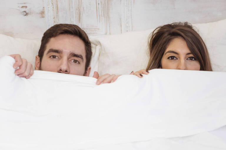 Casal de homem e mulher se escondendo debaixo do cobertor