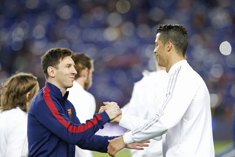 Messi, de uniforme azul escuro com uma faixa vermelha na manga, e Cristiano Ronaldo, de uniforme branco, cumprimentam-se antes de um Barcelona x Real Madrid, no Camp Nou, pelo Campeonato Espanhol