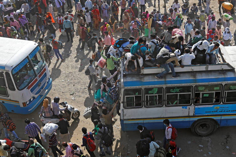 Trabalhadores tentam embarcar em ônibus lotados para retornar a seus vilarejos durante a quarentena, em Ghaziabad, arredores de Nova Déli, na Índia 
