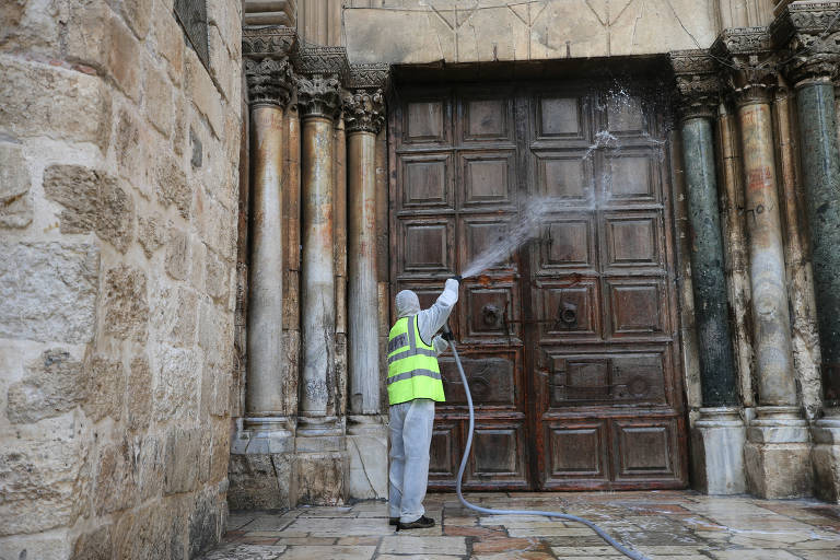 Trabalhador limpa a porta da Igreja do Santo Sepulcro, em Jerusalém, para evitar a propagação do coronavírus