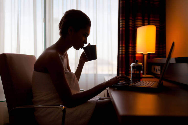 Mulher jovem em frente a computador em um quarto de hotel