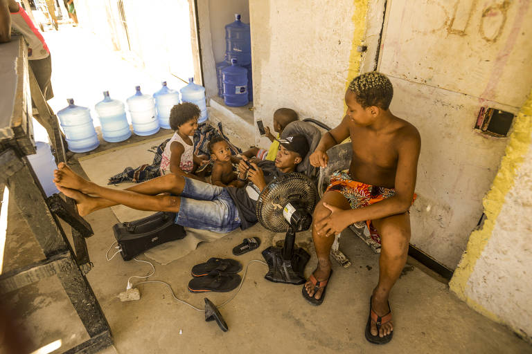 O calor impede que as pessoas se recolham a suas casas, onde às vezes vivem 12 pessoas; em uma das calçadas, um ventilador dá alívio a um adolescente e quatro crianças que se divertem no celular grudadas umas nas outras