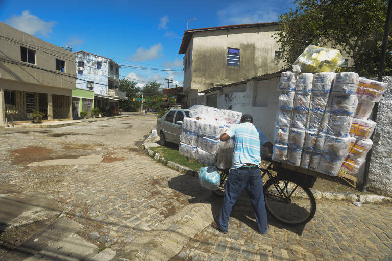 Em sua bicicleta, o entregador vai carregado com rolos de papel higiênico para abastecer um mercadinho local