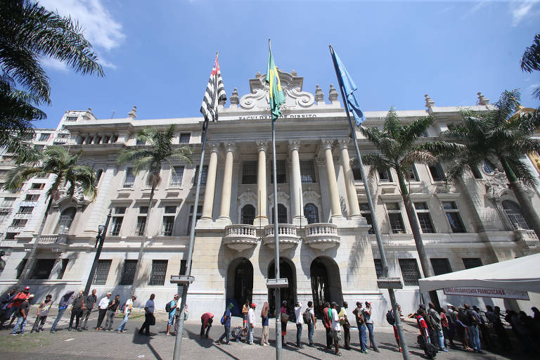Moradores de rua fazem fila para receber comida distribuída por padres franciscanos, em frente ao largo de São Francisco, no centro de SP