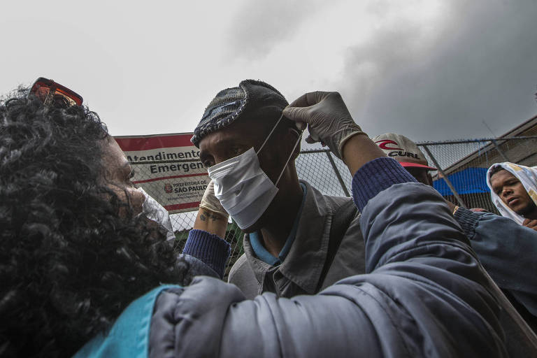 Agente de saúde coloca máscara em sem-teto durante o fechamento do serviço para usuários de drogas na cracolândia; ativistas reclamam que população ficará exposta ao novo coronavírus