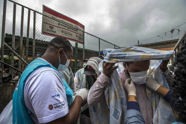 Agente de saúde coloca máscara em sem-teto durante o fechamento do serviço para usuários de drogas na cracolândia; ativistas reclamam que população ficará exposta ao novo coronavírus