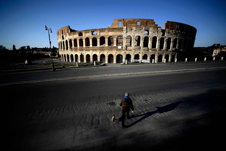 Homem caminha com cachorro na frente do Coliseu em Roma 