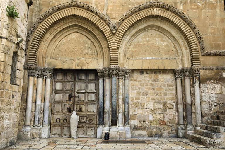 Peregrino vestido como Jesus aguarda em frente à Igreja do Santo Sepulcro, que foi fechada por causa da pandemia de coronavírus