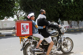 A delivery man wearing a protective face mask rides his motorbike with a boy, amid fear of coronavirus disease (COVID-19), in Sanaa