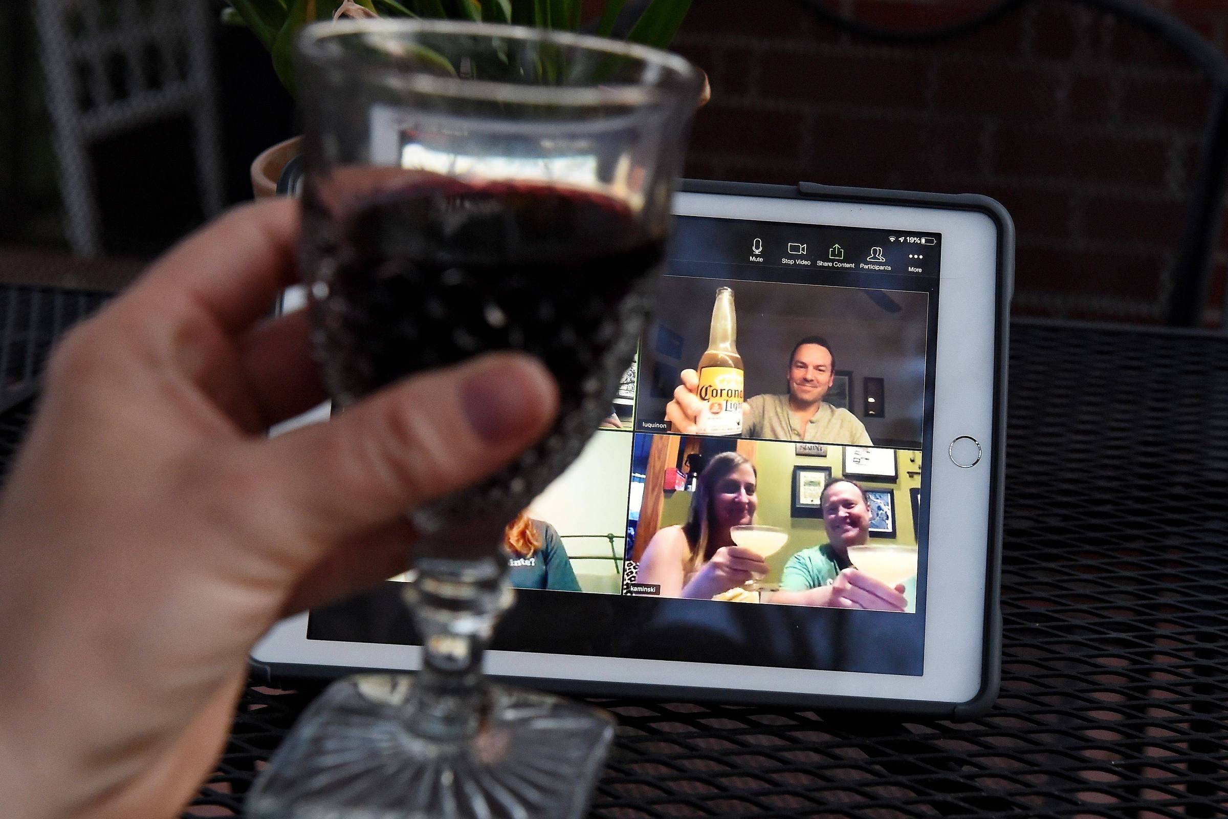 Mulher ergue copo de vinho em happy hour virtual com amigos nos EUA durante pandemia de coronavírus