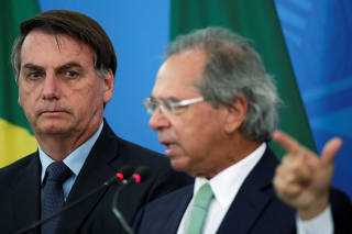 Brazil's President Jair Bolsonaro listens Brazil's Economy Minister Paulo Guedes during a media statement announcing economic measures, amid coronavirus disease (COVID-19) outbreak, in Brasilia