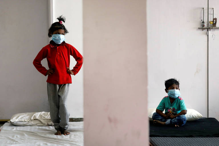 Filhos de trabalhadores migrantes usam máscaras protetoras dentro de um complexo esportivo transformado em abrigo em Nova Délhi, na Índia