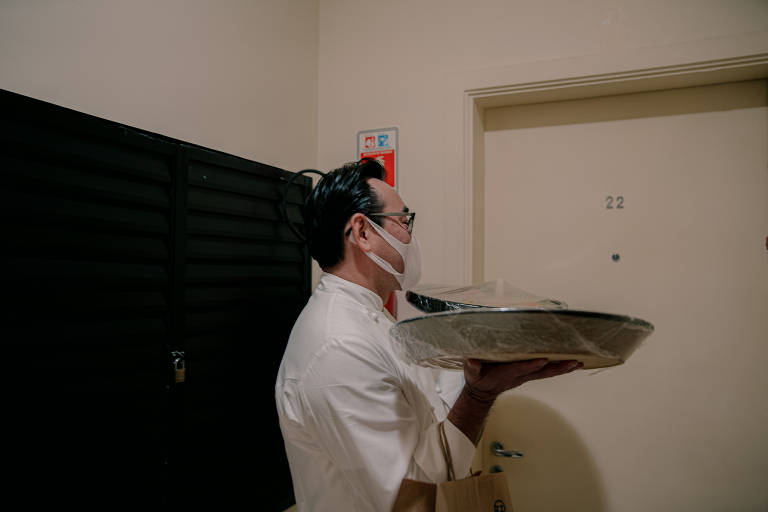 O chef usa máscara para fazer entrega para os clientes em louças feitas à mão;  no dia seguinte, ele retorna para recolher os utensílios