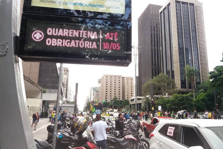 Manifestantes contra Doria e a favor de Bolsonaro passam por painel com aviso sobre isolamento social em São Paulo