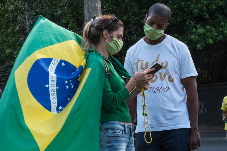 Manifestantes usam máscaras de proteção e exibem bandeira do Brasil ao final de uma carreata realizada em favor do fim do distanciamento e isolamento social, na avenida Niemeyer, bairro de São Conrado, na zona sul do Rio,  no sábado (18)
