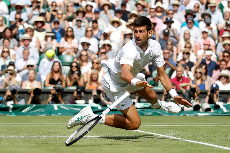 Djokovic se joga para alcançar uma bola na quadra de grama, observado pelo público