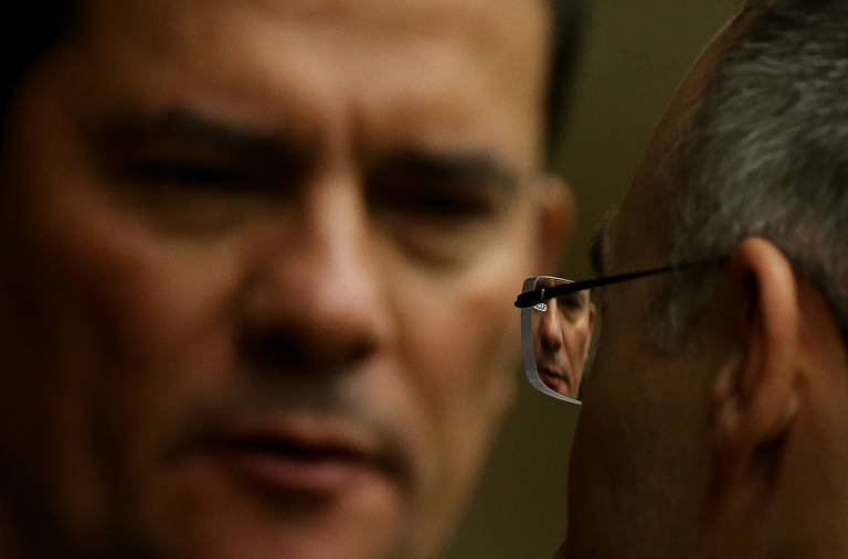 A imagem do ex-juiz e ex-ministro Sergio Moro é refletida nos óculos do advogado-geral da União, André Mendonça, na cerimônia de abertura do ano do Judiciário