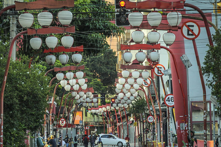 Imagem mostra rua sem pedestre e com seus postes que imitam lanternas japonesas (são astes vermelhas curvas com três luminárias brancas arredondadas cada)