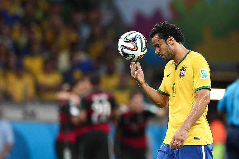 Fred carrega a bola enquanto os alemães comemoram gol contra o Brasil na semifinal da Copa de 2014