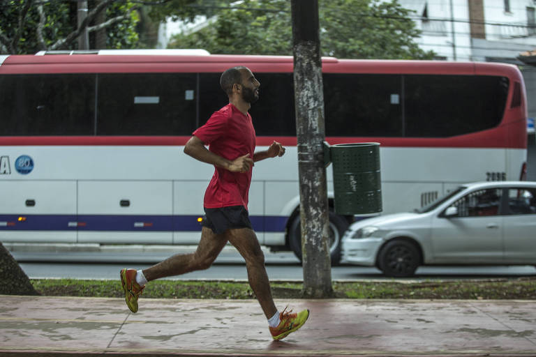Homem se exercita nas ruas de Perdizes (zona oeste de São Paulo) durante a pandemia de coronavírus; homem de short e camiseta passa correndo numa calçada; ao fundo veem-se um táxi e um ônibus, na rua