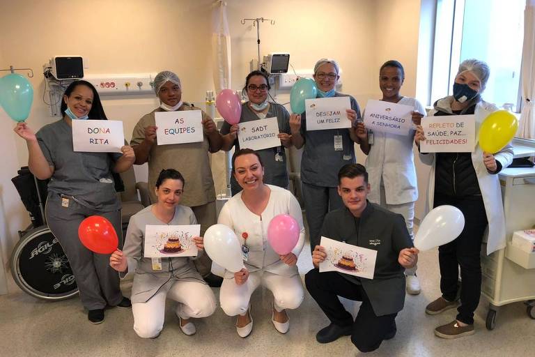 profissionais da saúde seguram cartazes e balões coloridos em uma sala de hospital