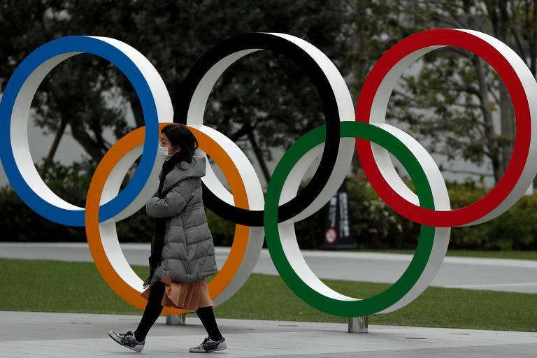 A mulher com máscara protetora passa em frente aos anéis olímpicos em Tóquio