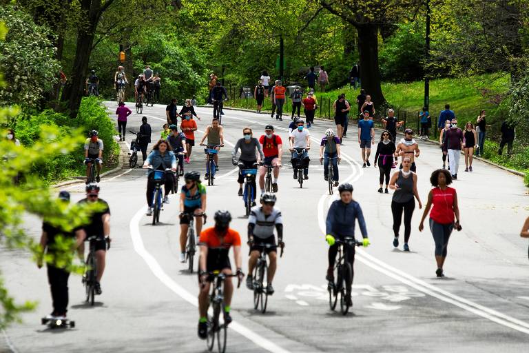 Ciclistas são vistos em primeiro plano pedalando pelo Central Park