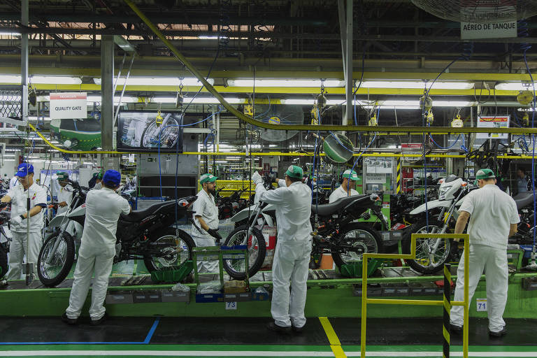 Homens trabalham na montagem de motos usando macacões brancos
