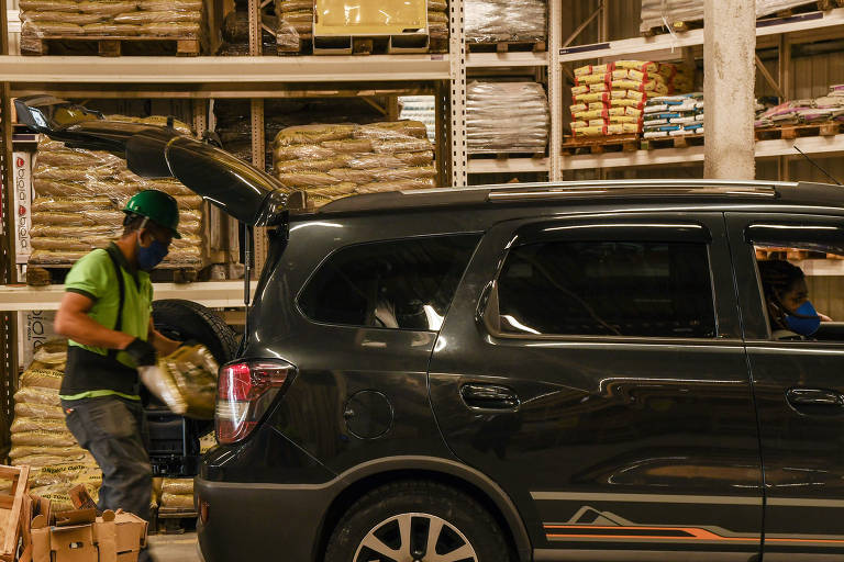 Lojas e shoppings fazendo drive-thru; Funcionário coloca produtos adquiridos no porta-malas de um cliente