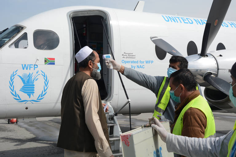 Funcionários e passageiros que embarcam em avião do Serviço Aéreo Humanitário das Nações Unidas (Unhas, na sigla em inglês) em Cabul, no Afeganistão, têm a temperatura medida em meio à pandemia de coronavírus