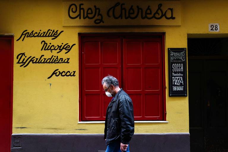 Um homem usando máscara passa por um restaurante fechado em uma rua vazia na cidade de Nice, na Riviera Francesa, no sul da França. O país está no 54º dia de um bloqueio contra o novo coronavírus 