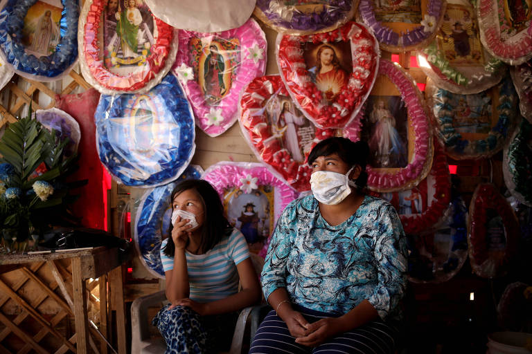 Rosa Leyva (dir.) e sua sobrinha Viridiana aguardam clientes em sua barraca, onde ela vende arranjos de flores de plástico e imagens religiosas, fora do cemitério de San Rafael, em Ciudad Juarez, no México