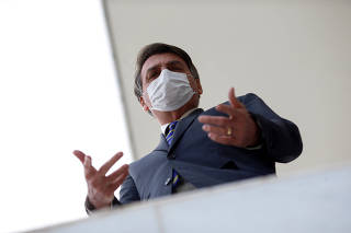 Brazil's President Jair Bolsonaro wearing a protective mask gestures as he speaks with journalists, amid the coronavirus disease (COVID-19) outbreak, at the Planalto Palace, in Brasilia