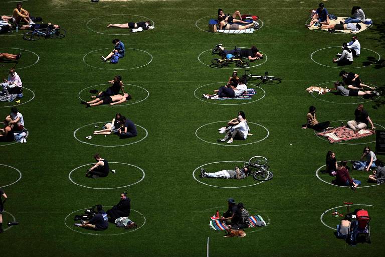 Moradores deitam na grama do Domino Park, no Brooklyn (Nova York); círculos brancos foram riscados no chão para demarcar o espaço de distanciamento social 