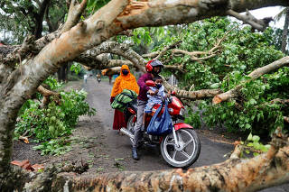 A man with a child ride on motorbike in the street blocked by trees that were uprooted by the cyclone Amphan, in Satkhira