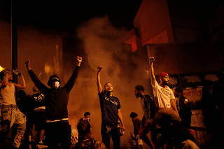 Protesters gather around after setting fire to the entrance of a police station as demonstrations continue in Minneapolis
