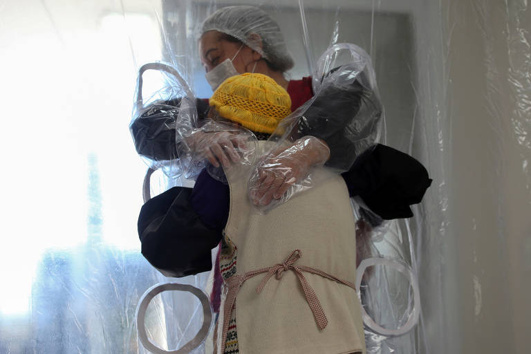 Irmãs se abraçam por meio de uma cortina de plástico em uma casa de idosos em São Paulo