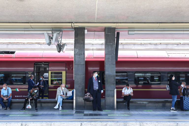 Pessoas de máscara na estação de trem Termini, em Roma, e mantêm distância