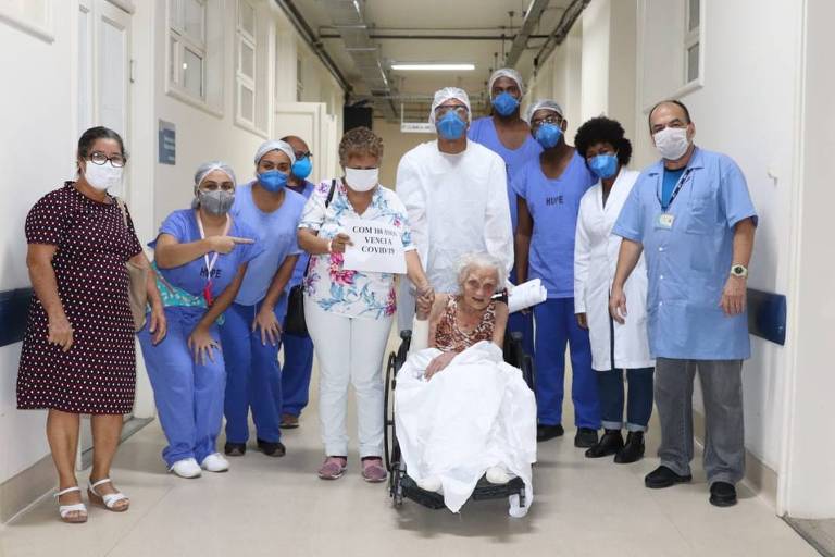mulher idosa em cadeira de rodas acompanhada por equipe de hospital usando roupas azuis